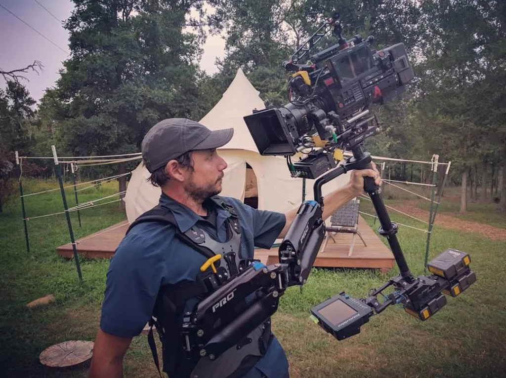 Michael “Doc” Deitch wearing his Steadicam rig with a cinema camera in front of a canvas bell tent in the trees