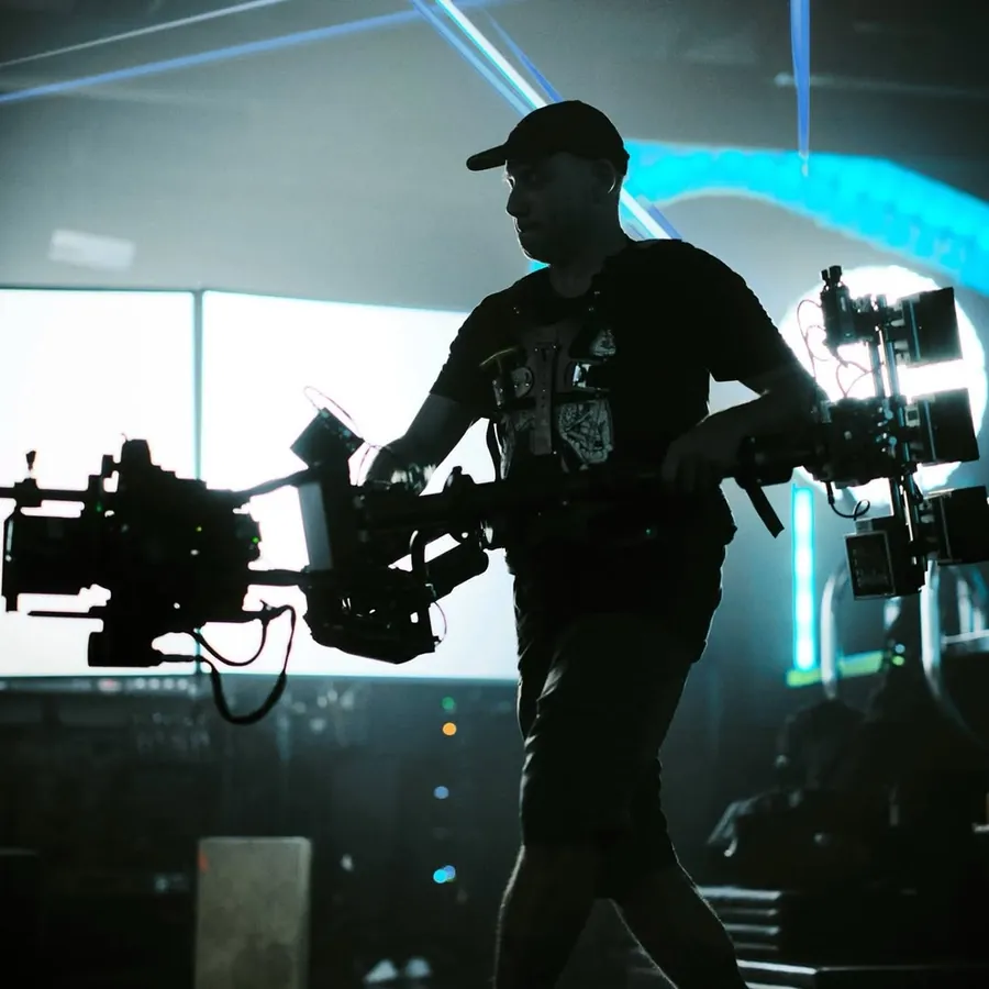 Silhouette of Michael Deitch carrying an ARRI Trinity 2 rig in front of bright screens and blue light